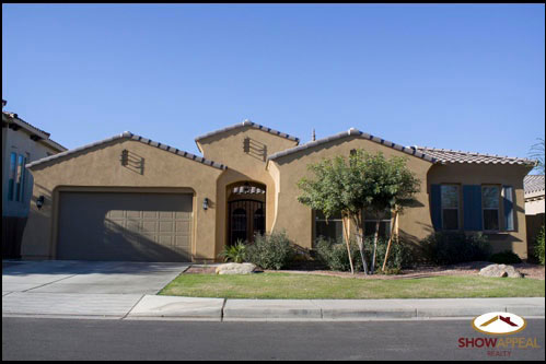 a nice two story brown stucco house with plants on the front