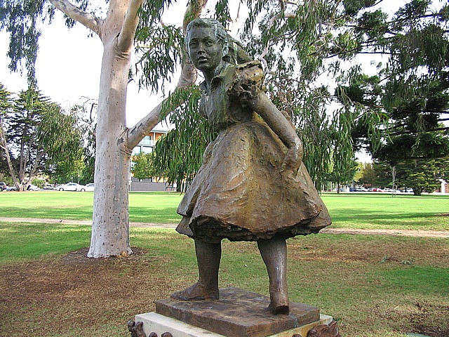 a little girl statue standing under a tree