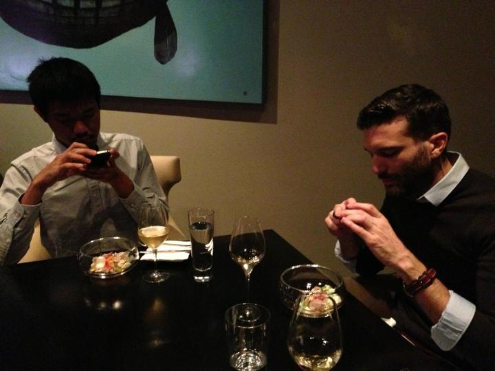 two men looking at their phones while at a table with food