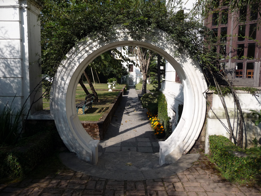 an outdoor garden features white circular arches and stone pavement