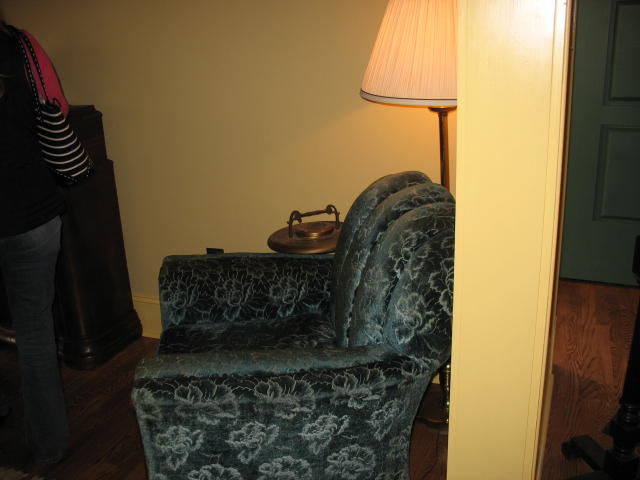 a blue velvet armchair with foot rest underneath a table lamp