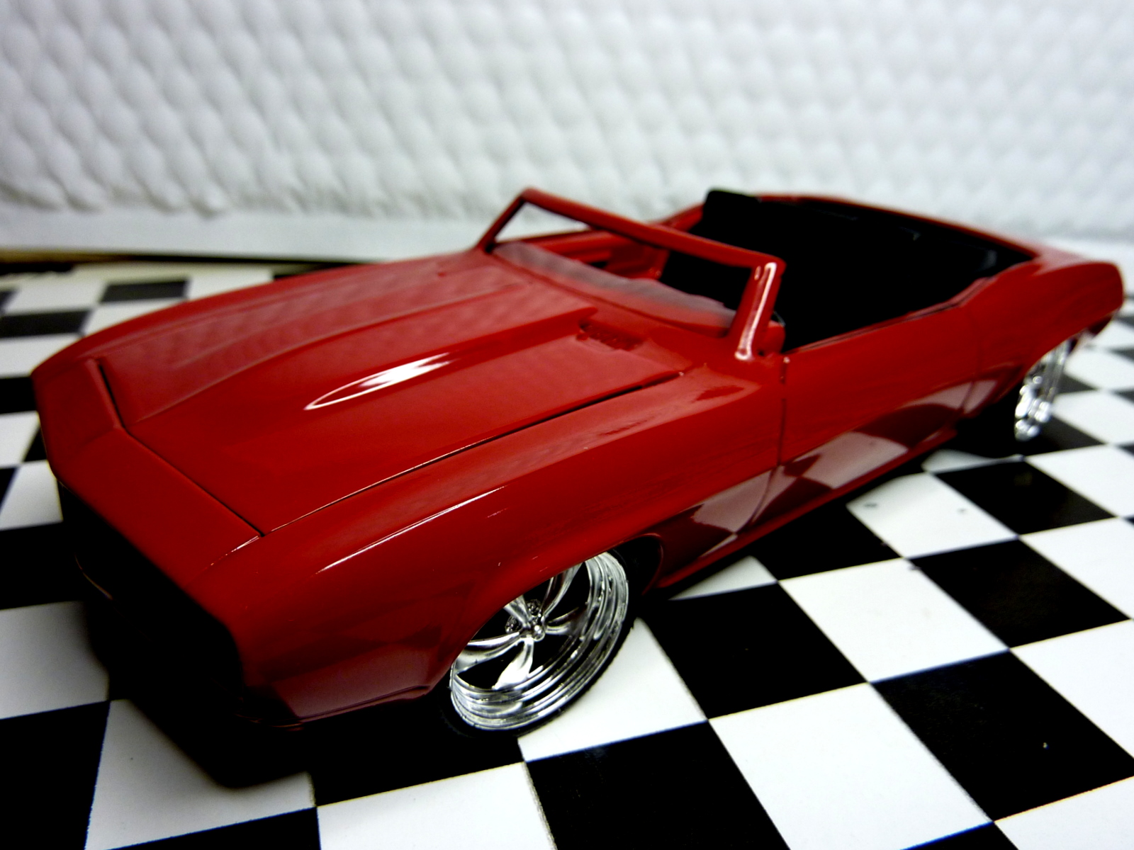 a red toy car sitting on top of a black and white checkered floor