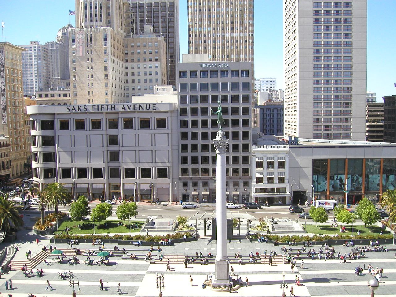 people walk through the plaza with tall buildings