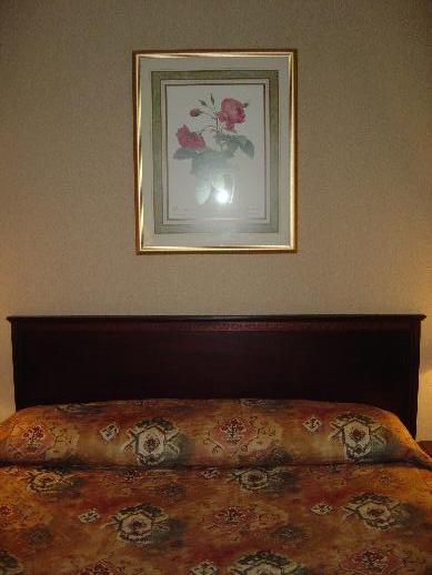 bed with orange comforter and brown bed spread with a framed picture of flower print
