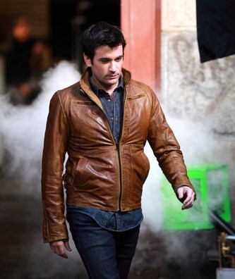 a man wearing a jacket and jeans holding a cigarette