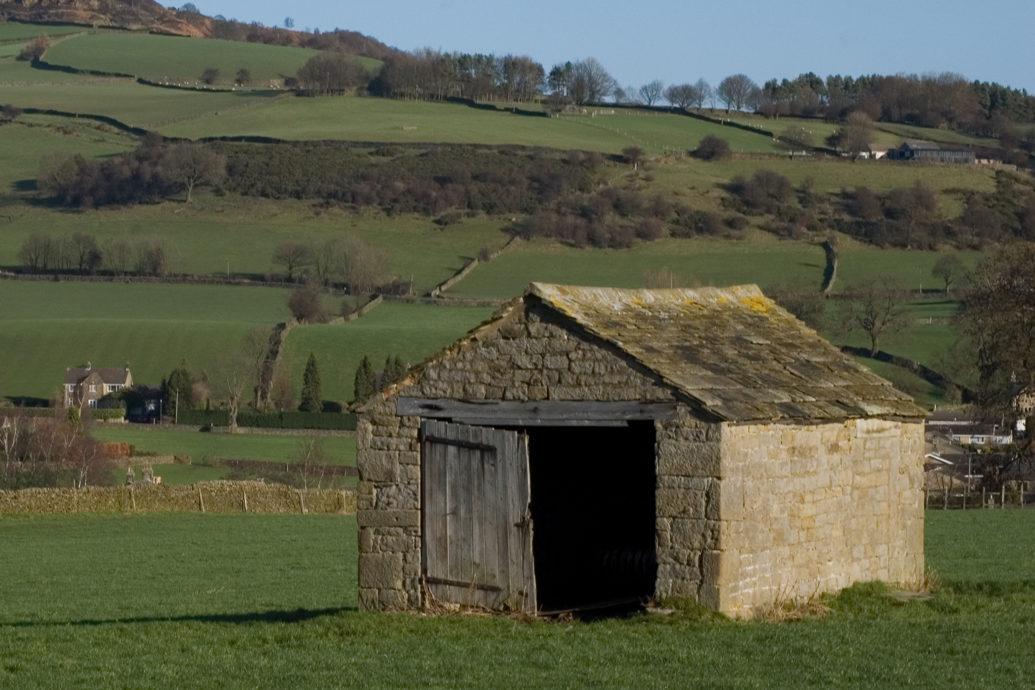 a stone shed with a green rolling hills behind it