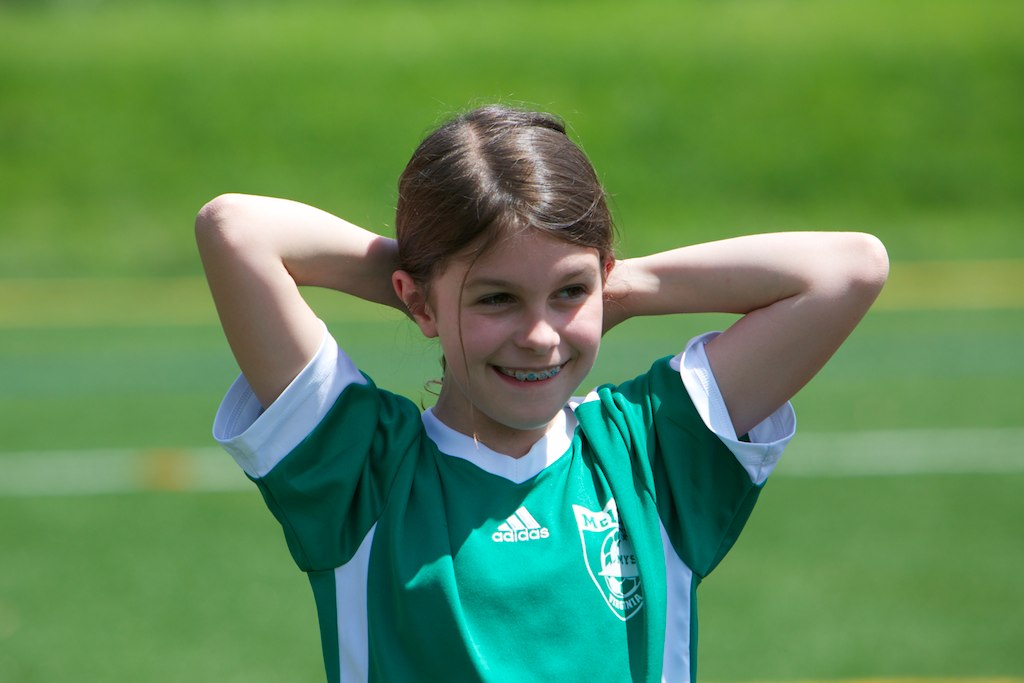 a girl in green jersey standing next to a soccer field