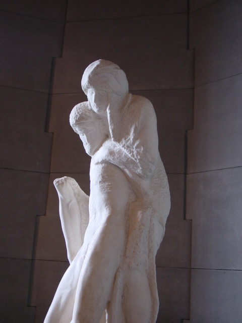 a white statue holding another figure in front of a wall