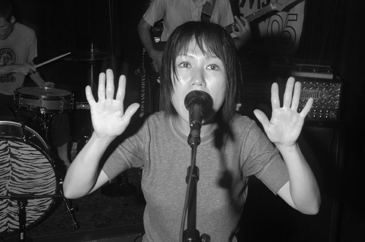 a girl with one hand up to her mouth as a man plays guitar in the background