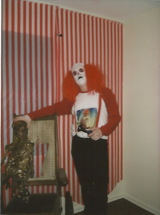 a man wearing a clown mask stands next to a chair