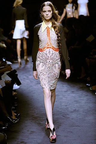 a woman walks down a runway in an orange and white outfit