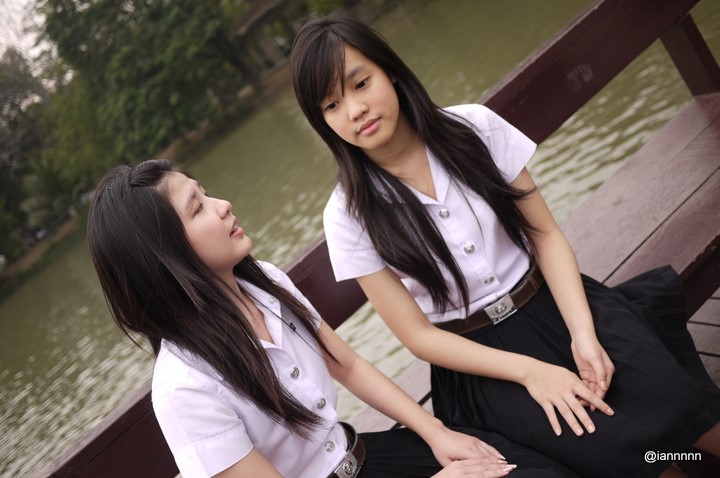 two asian girls sit on a bench looking at each other