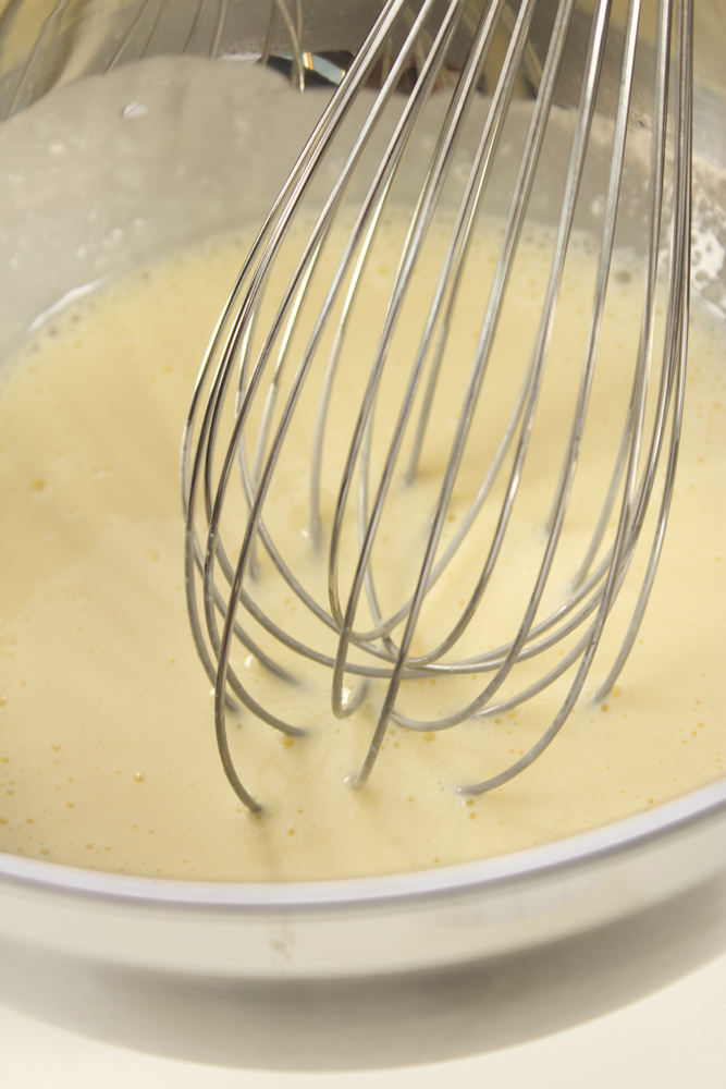 a mixing bowl with a whisk next to another bowl full of batter