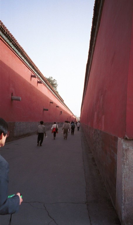 a guy standing next to red buildings and looking away