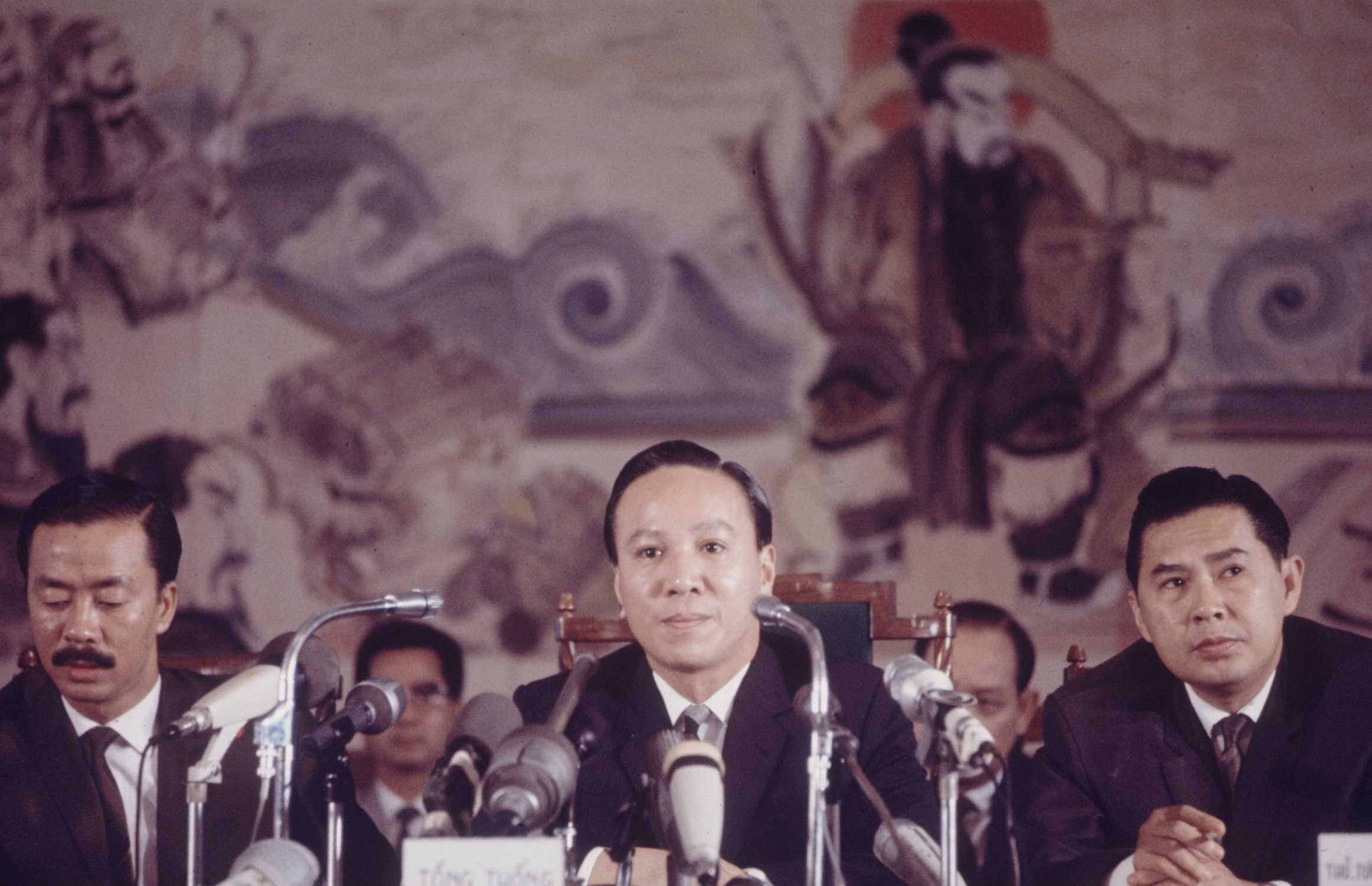 a group of men sitting at a desk with microphones