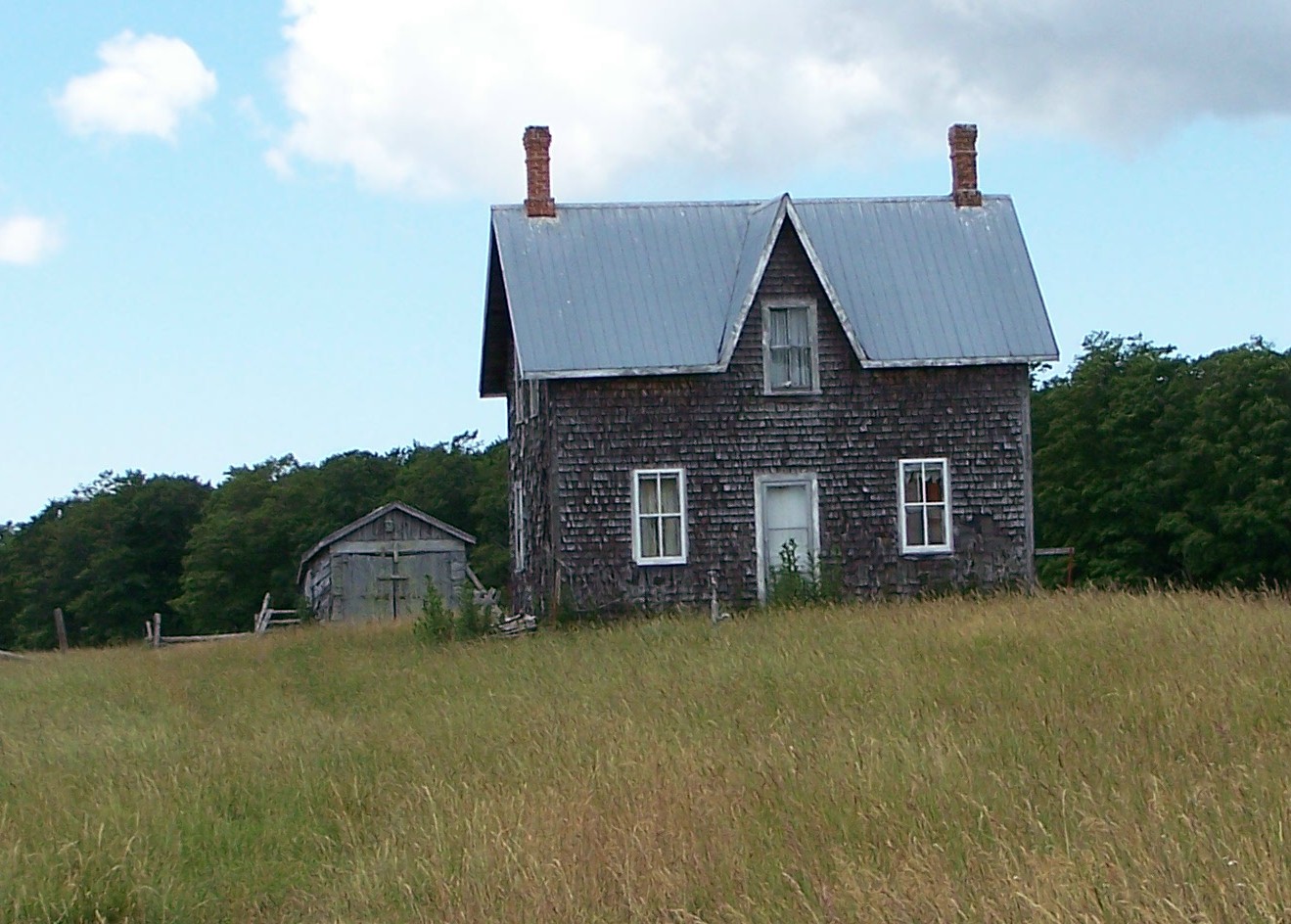 there is an old wooden house in the middle of a grassy field