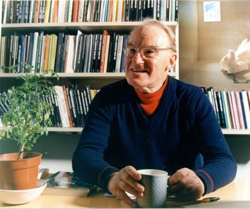 an older man sitting at a desk with a cup of coffee