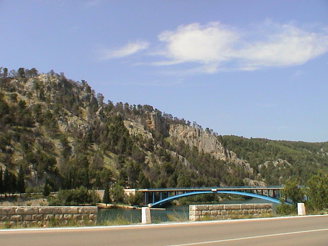 a blue bridge over water next to a lush green mountain