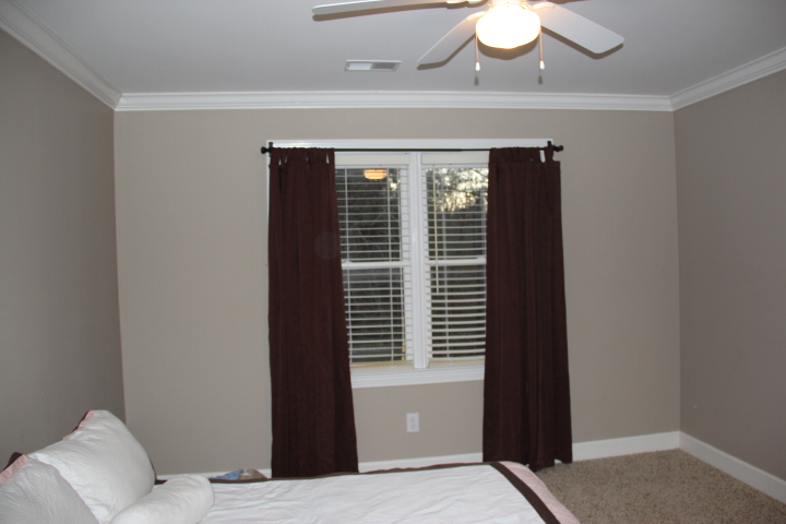 a small bedroom with white and brown curtains and a brown light fixture