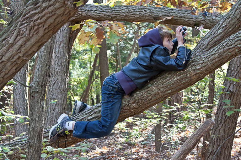a boy laying on a tree nch using a digital camera