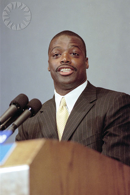 a man sitting at a podium wearing a suit and tie
