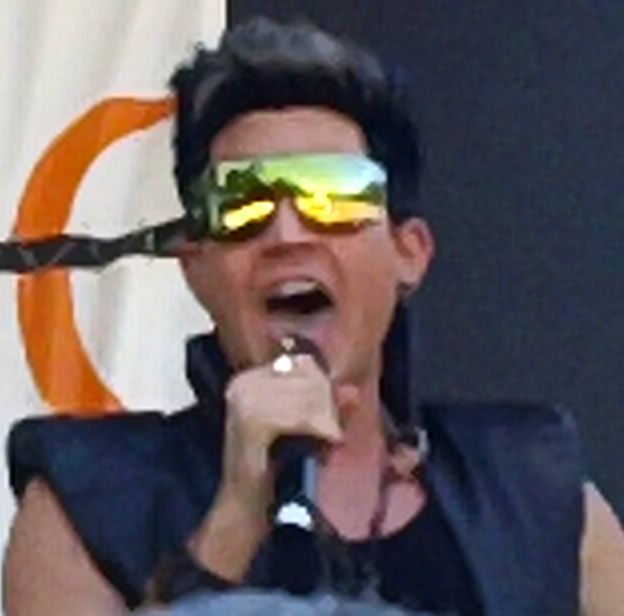 the singer holds up a microphone while wearing shades