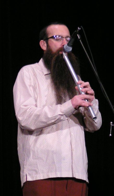 man with long, curly hair and beard holding an instrument
