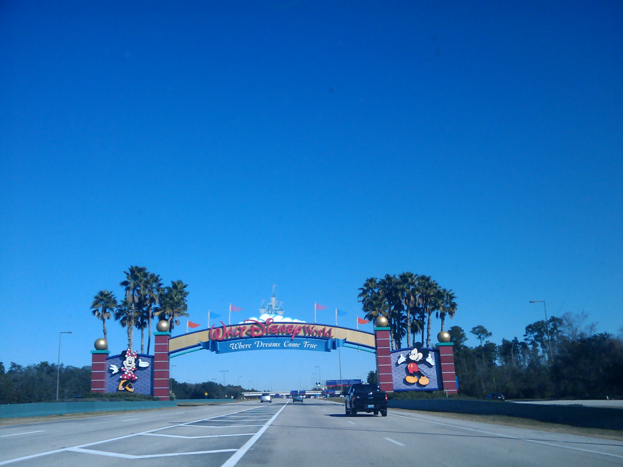 cars driving underneath a very tall colorful sign