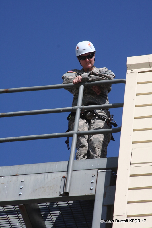 a male in military fatigues leaning on a metal rail with safety equipment