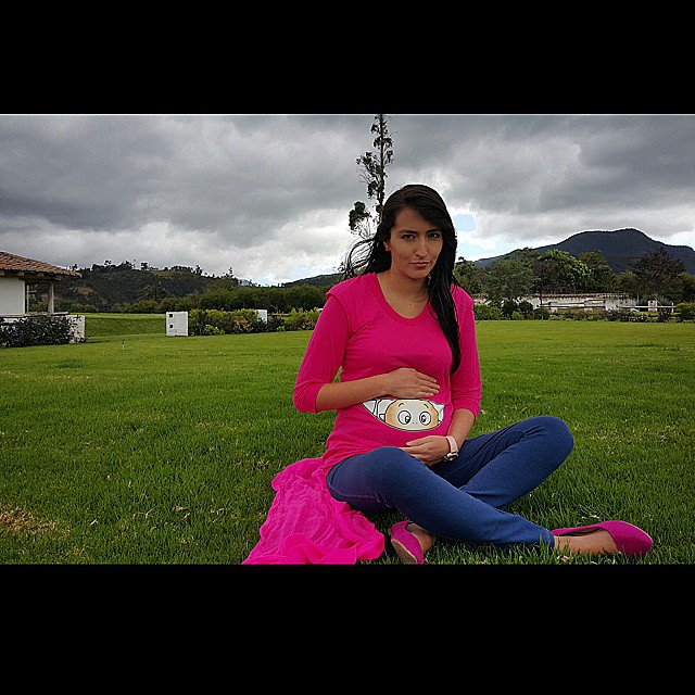 woman sitting on grass with cell phone, pink shirt and jeans
