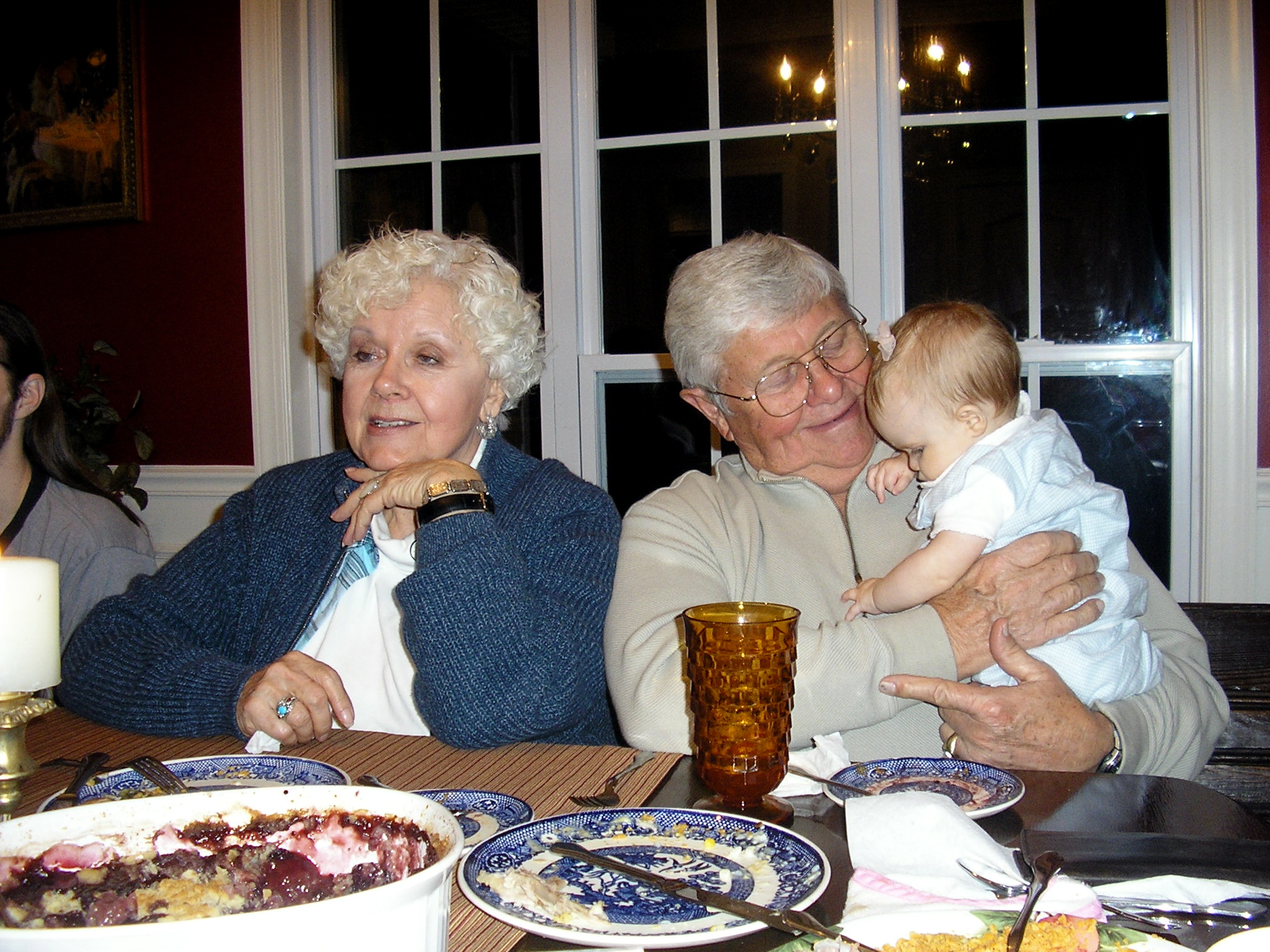 a woman holding her baby sitting at a dinner table with other people