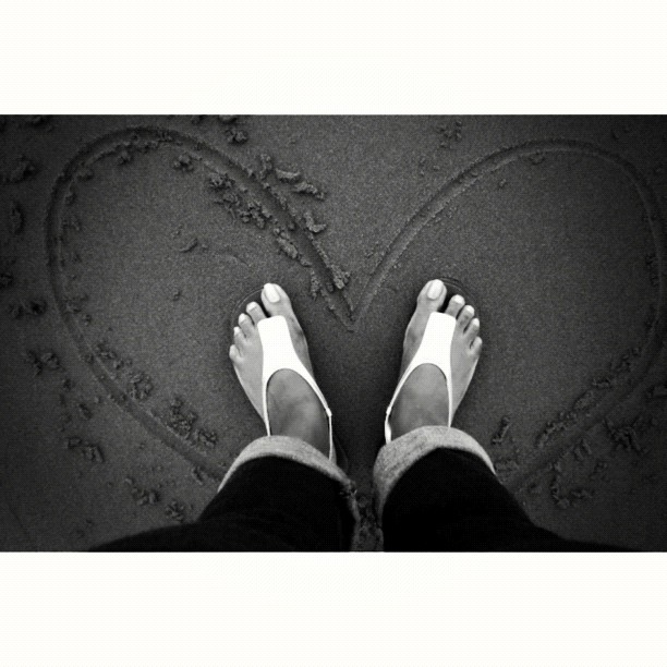 a person standing on a beach, with heart - shaped words and footprints