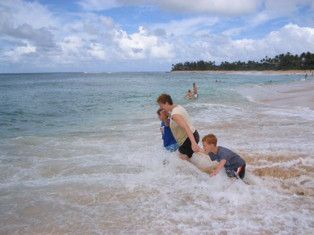 two children play with the waves while their parent watches them