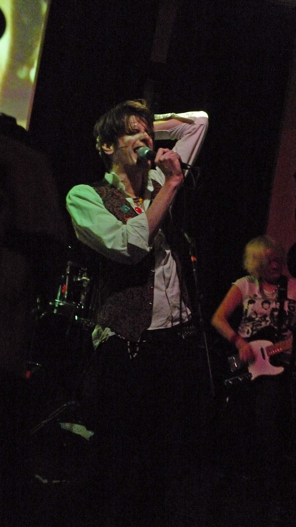 man in green shirt singing into microphone and two other men playing instruments