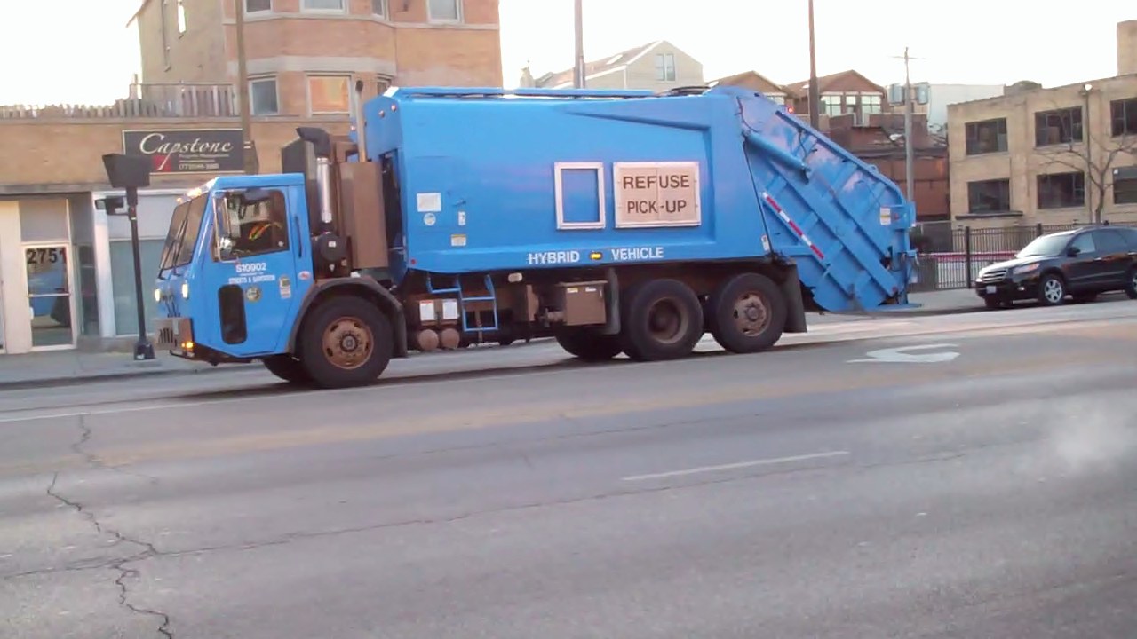 a blue garbage truck drives down the road