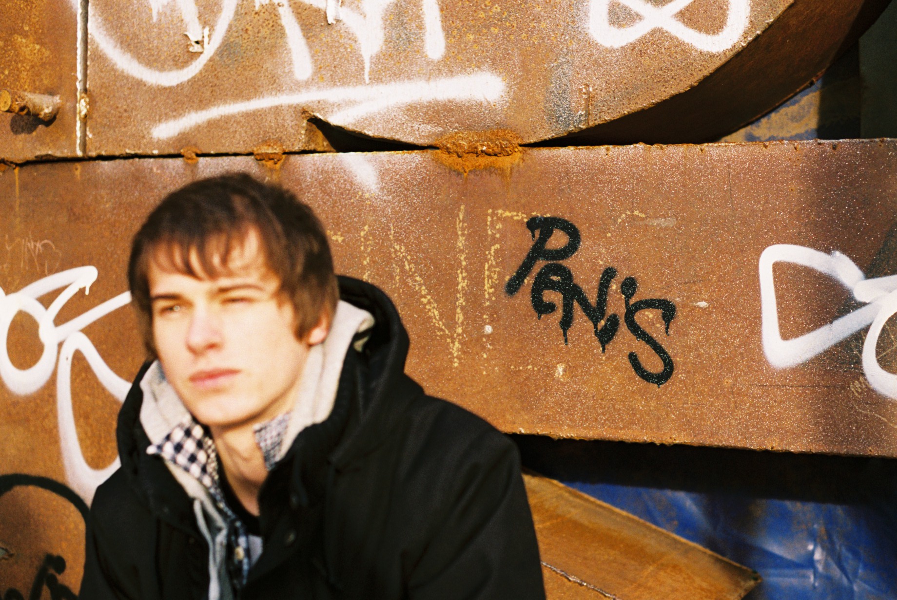 a young man with brown hair is standing in front of graffiti