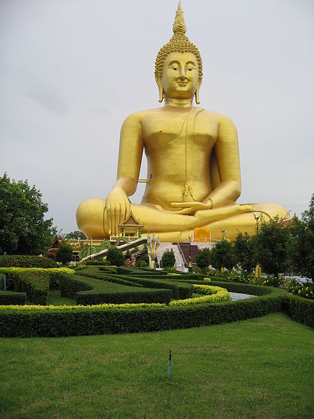 large golden statue of a buddha seated on a bench in a large, formal garden