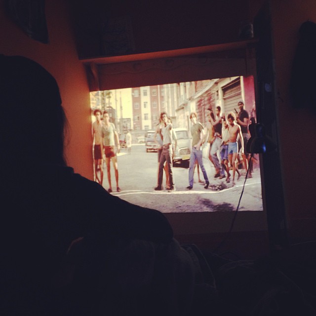 a man is holding his camera in front of a tv screen that shows a gang of people walking down the street