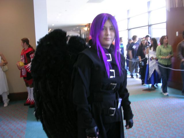 person with purple hair wearing black costume and with long black hair in the hallway with a crowd
