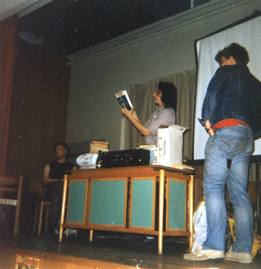 two men are standing in the living room next to an old television and a desk