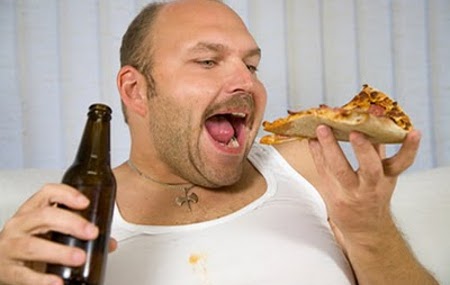 man sitting on a couch eating a slice of pizza and holding beer