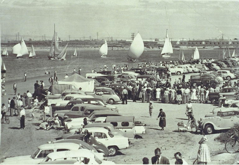 many people standing near many old cars at the beach