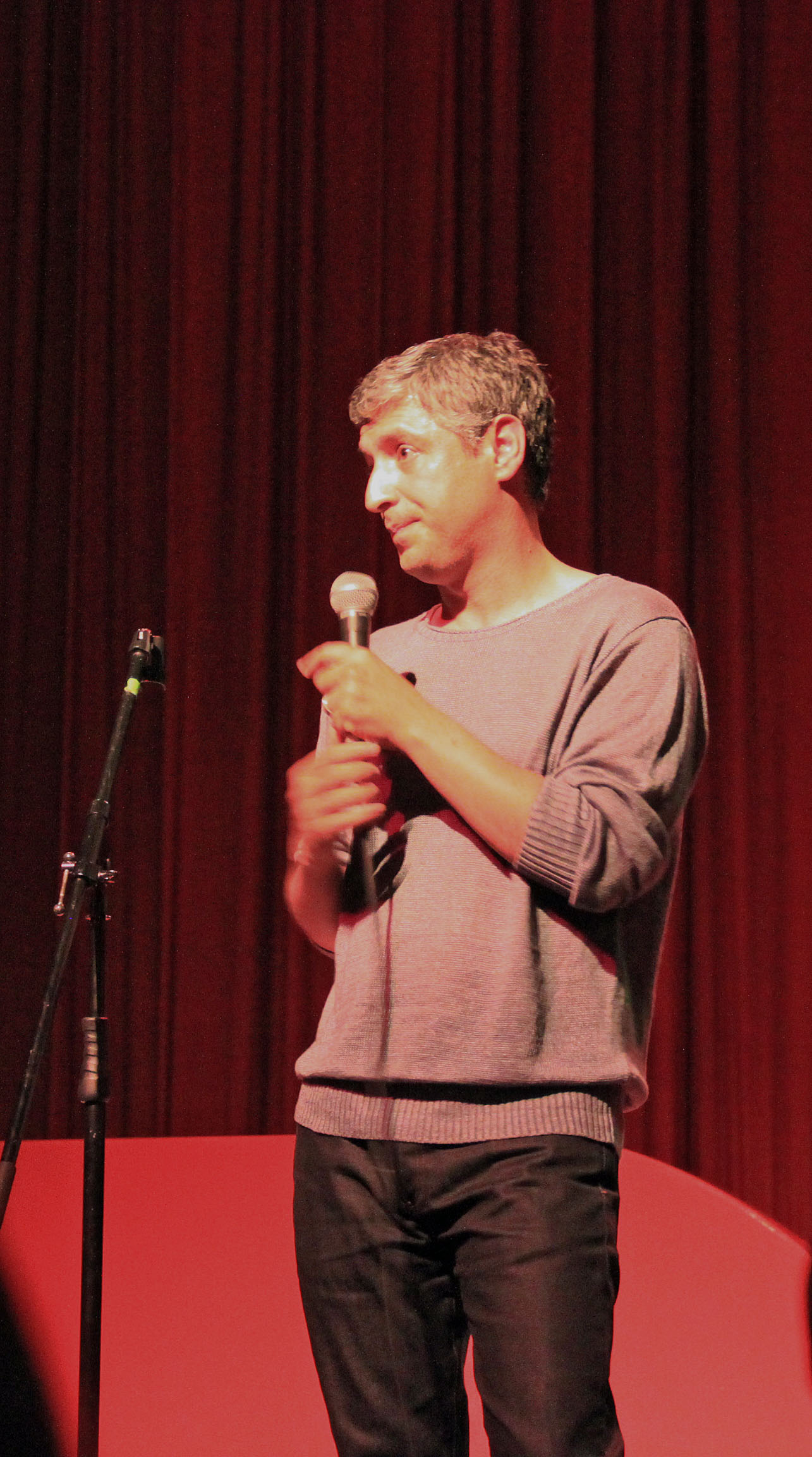 a man speaking with his microphone in front of a red curtain