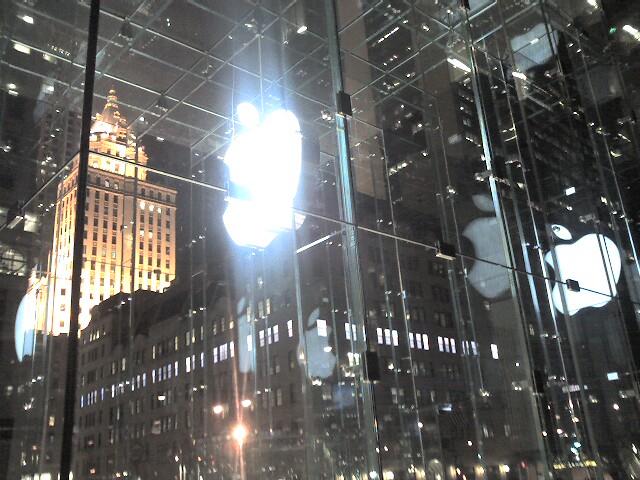 a glass apple store and an illuminated skyscr at night