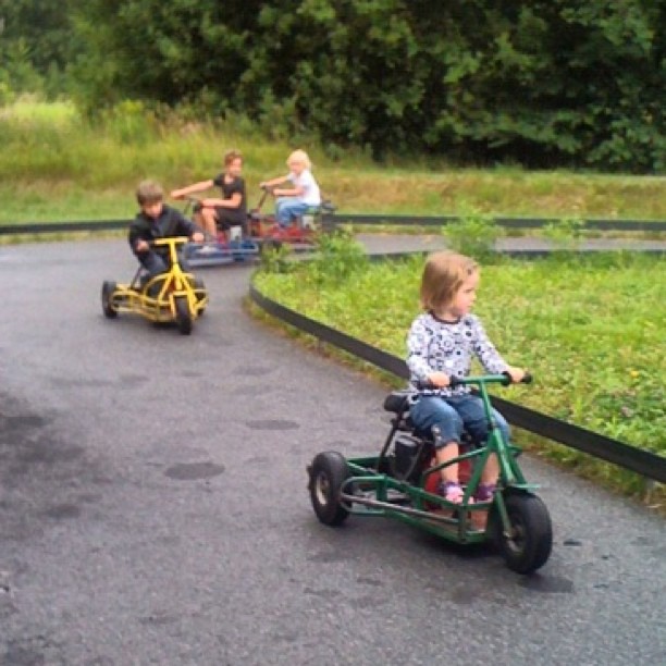 two children ride two small motorized vehicles down a paved road