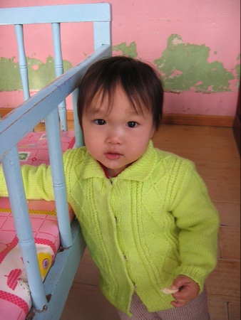 a toddler standing next to a cot on the floor