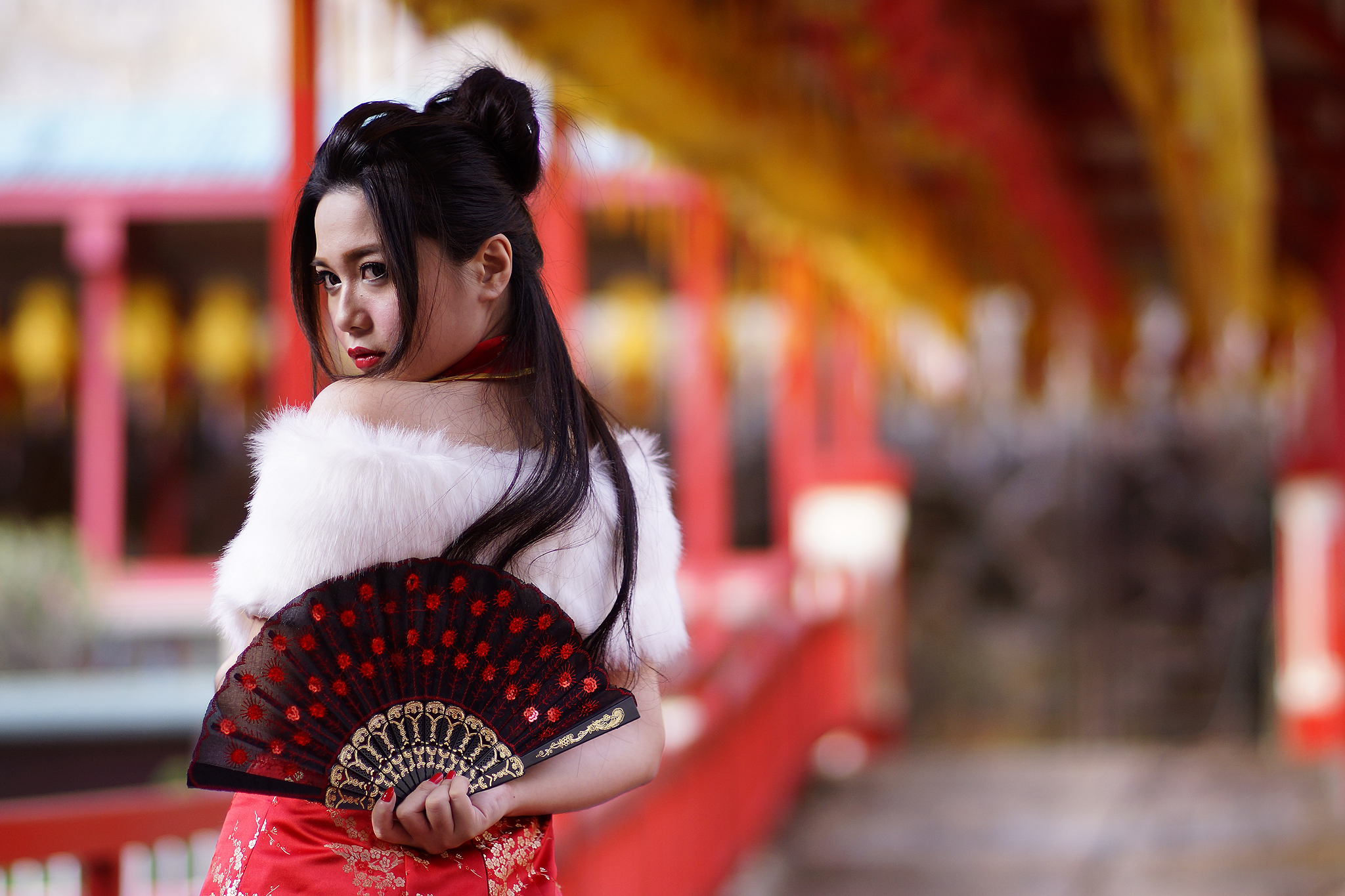 an oriental woman in a red dress stands with a fan