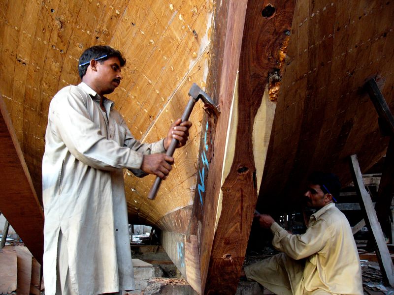 two men are working on wood in front of a boat