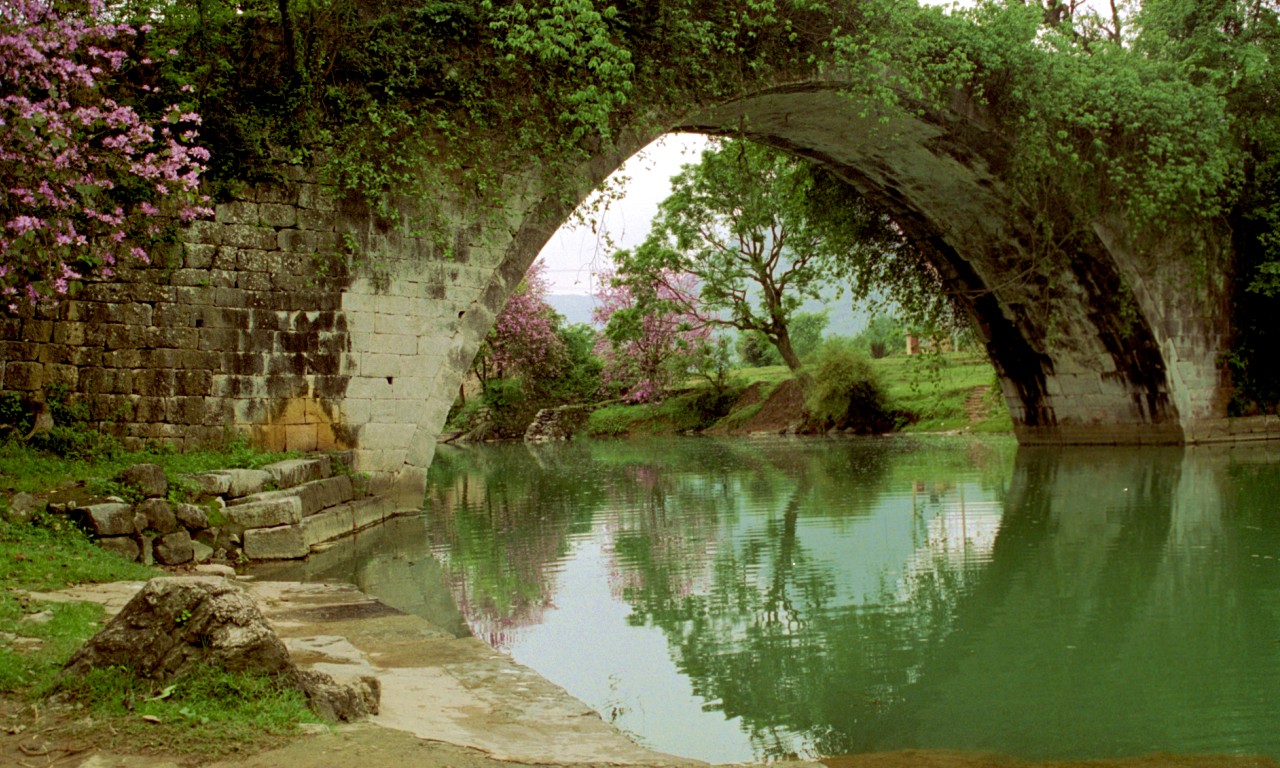 an arched stone bridge over a green river