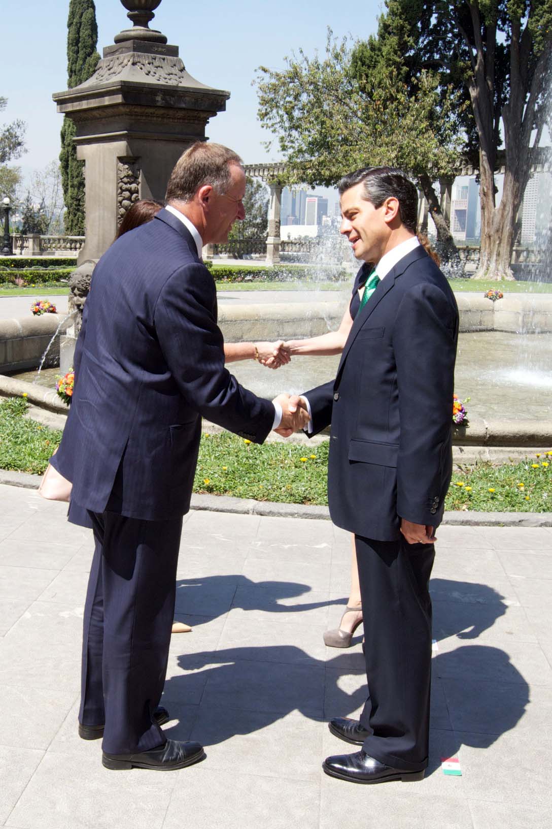 two men in suits shake hands at an open fountain